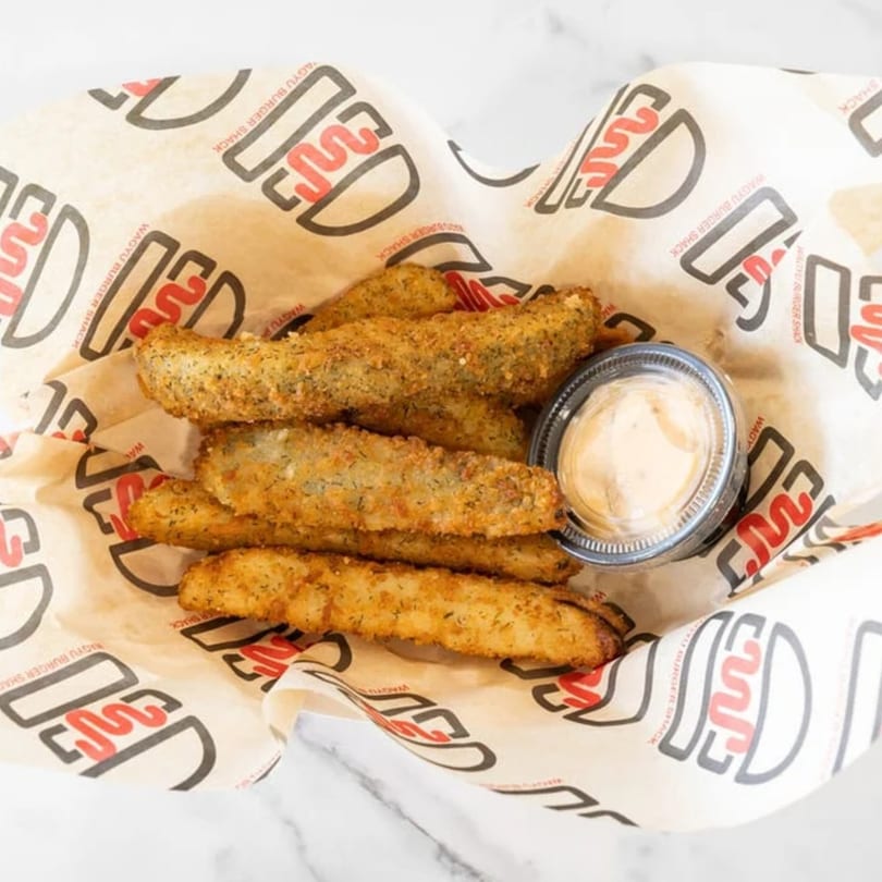 Wagyu Burger Shack fried pickles in a branded paper-lined basket with a side of dipping sauce.