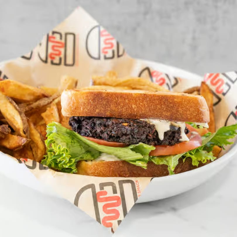 Wagyu Burger Shack's burger with a dark patty, lettuce, tomato, and sauce, served with fries.