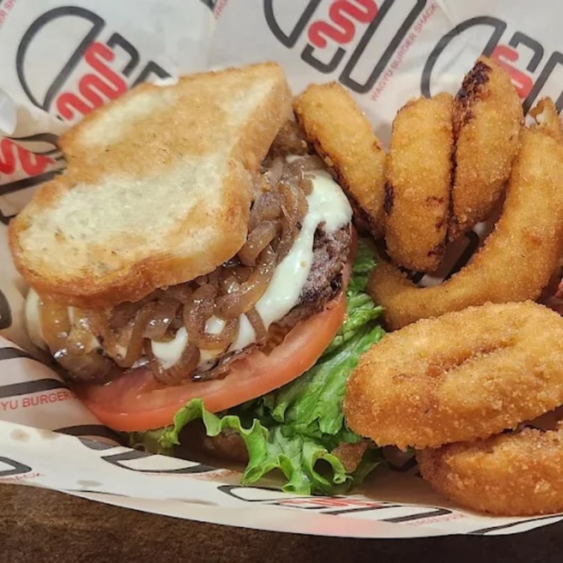 Wagyu Burger Shack burger with caramelized onions, melted cheese, tomato, lettuce, and a side of onion rings.